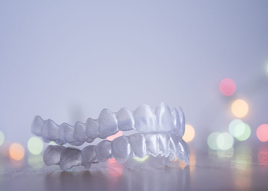 Upper and lower Invisalign aligners on a flat surface with multi colored lights in the background