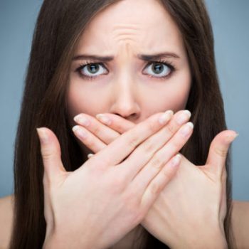 A woman with dark hair covering her mouth with both hands, looking worried