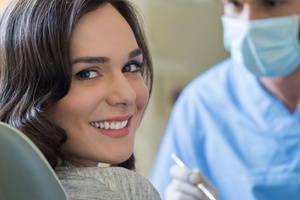 A woman with dark hair looking over her right shoulder at the camera with a dentist in the background