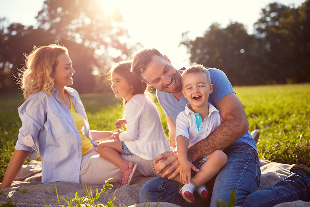 A young family sitting on a blanket in the grass, smiling and having fun