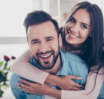Smiling woman embracing smiling man from behind